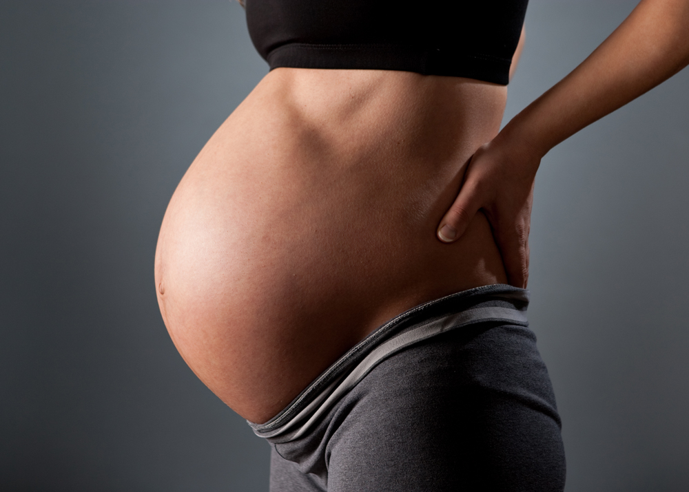 A side profile photo of a pregnant woman with a grey backdrop